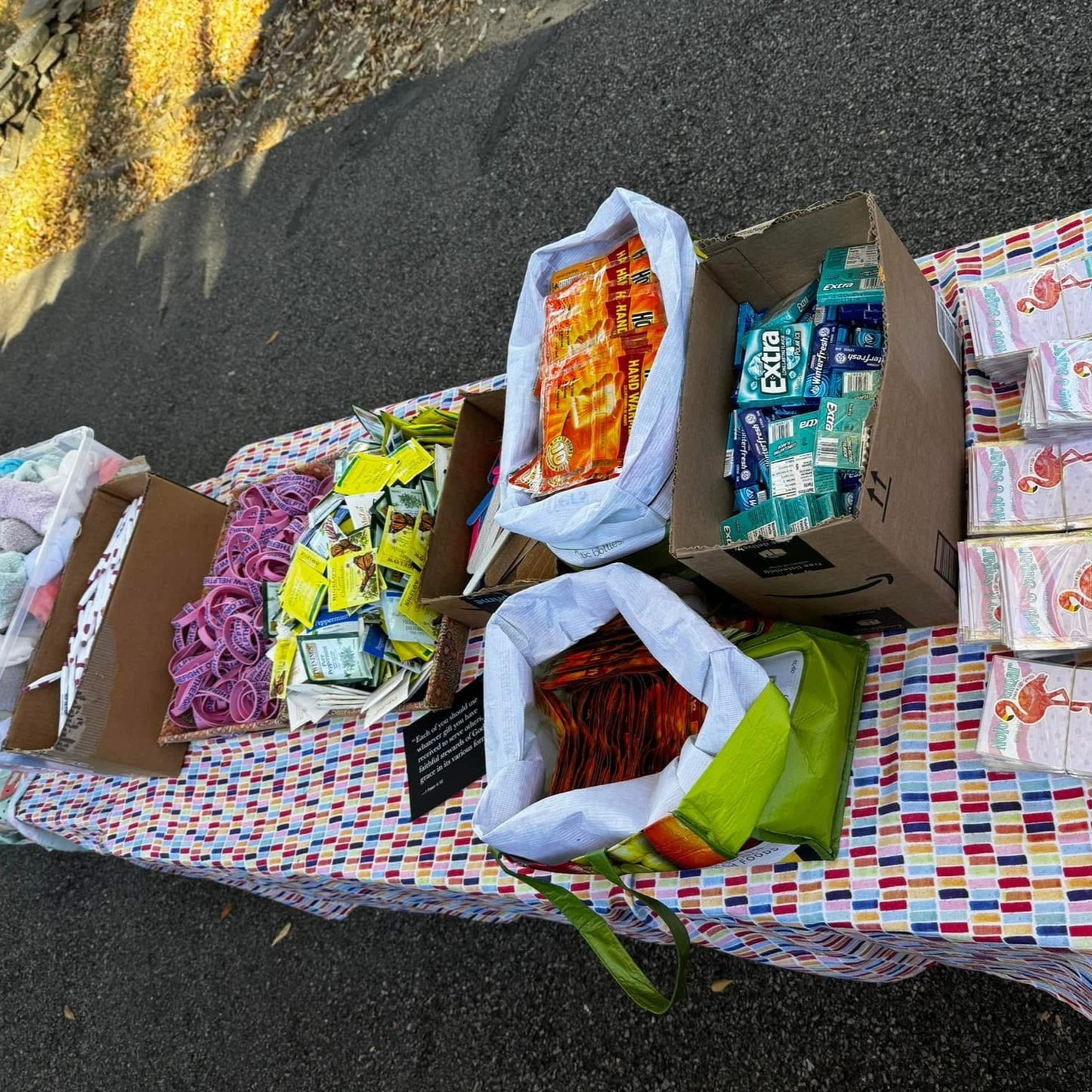 Collection of boxes and bags with various items on a colorful blanket outdoors.